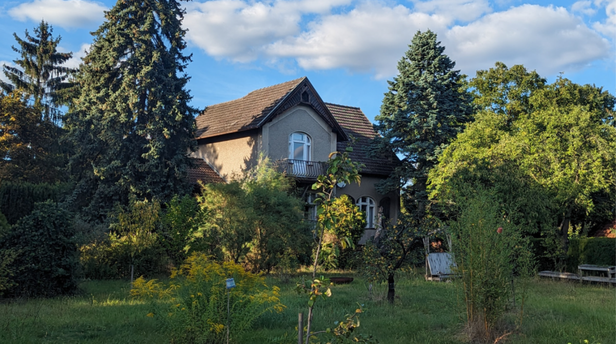 Blick auf das Gründerzeithaus durch Bäume und Sträucher des Selbstversorgergrundstückes